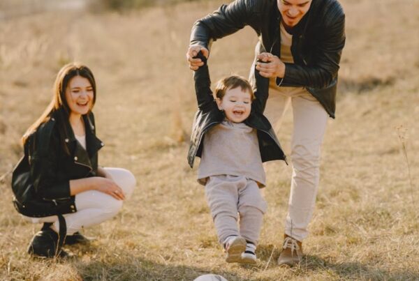 Family playing ball with their son in a dried grassy meadow under noon light during autumn, enjoying their time together.