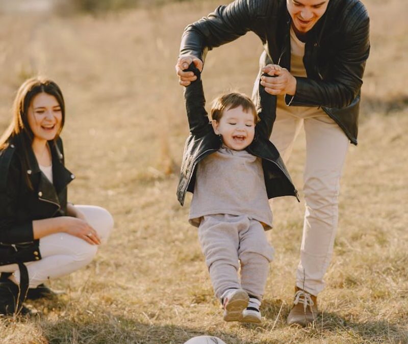 Family playing ball with their son in a dried grassy meadow under noon light during autumn, enjoying their time together.