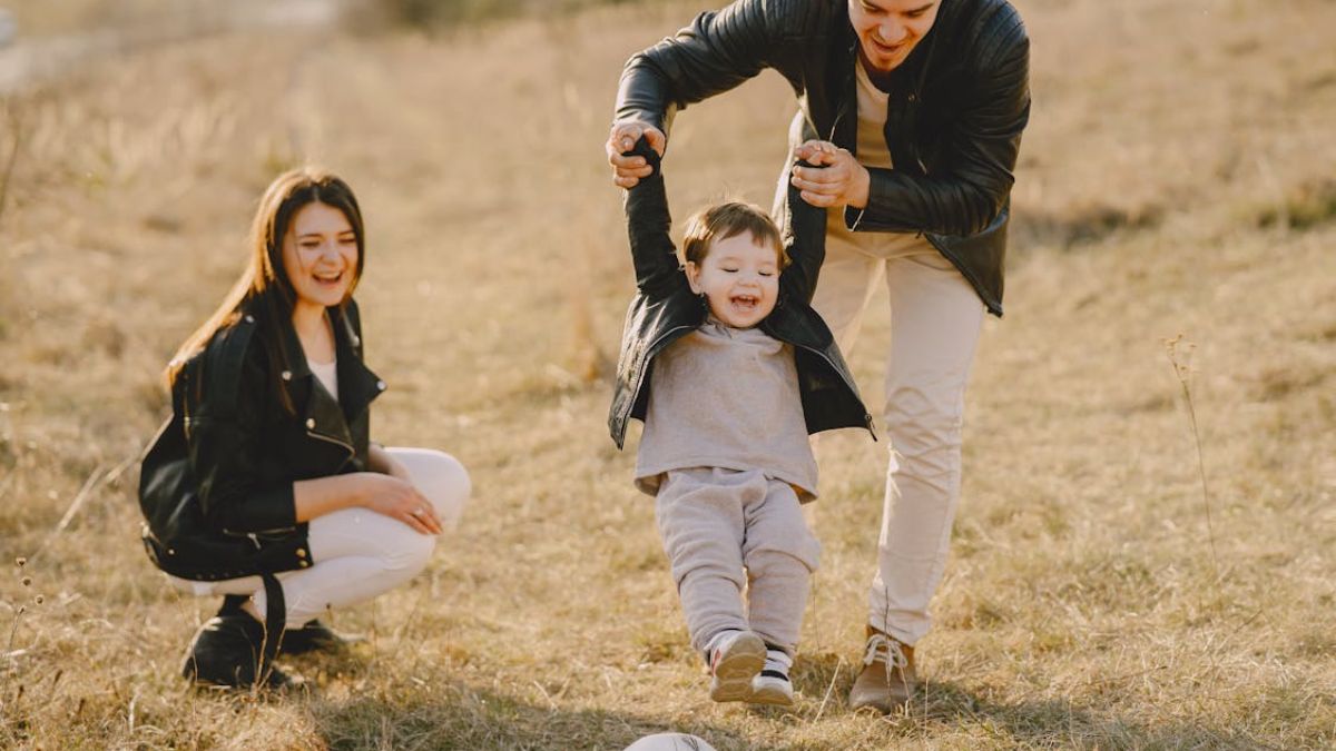 Family playing ball with their son in a dried grassy meadow under noon light during autumn, enjoying their time together.