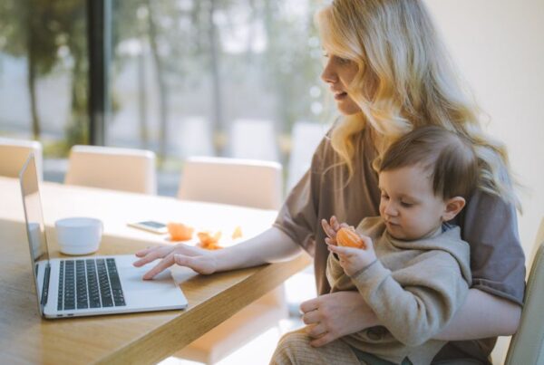 Blonde woman holding her child at a dinner table in a sunlit room while browsing ABA therapy centers.