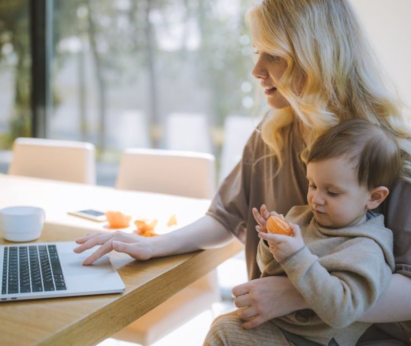 Blonde woman holding her child at a dinner table in a sunlit room while browsing ABA therapy centers.