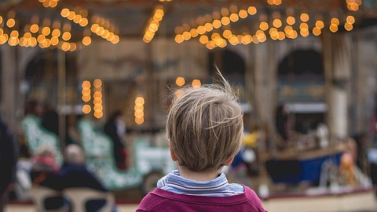 A little boy playing in the park, looking at a carousel in the soft afternoon light.