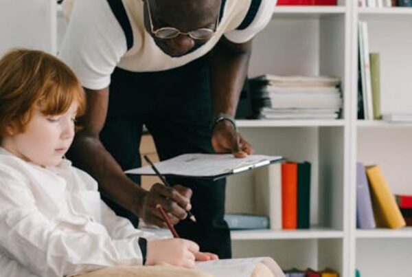 A therapist leaning over a boy, guiding him in ABA therapy in a sunlit room, looking focused.