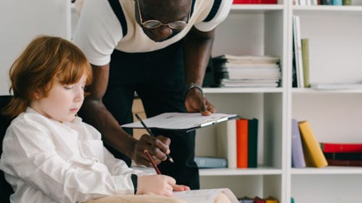 A therapist leaning over a boy, guiding him in ABA therapy in a sunlit room, looking focused.