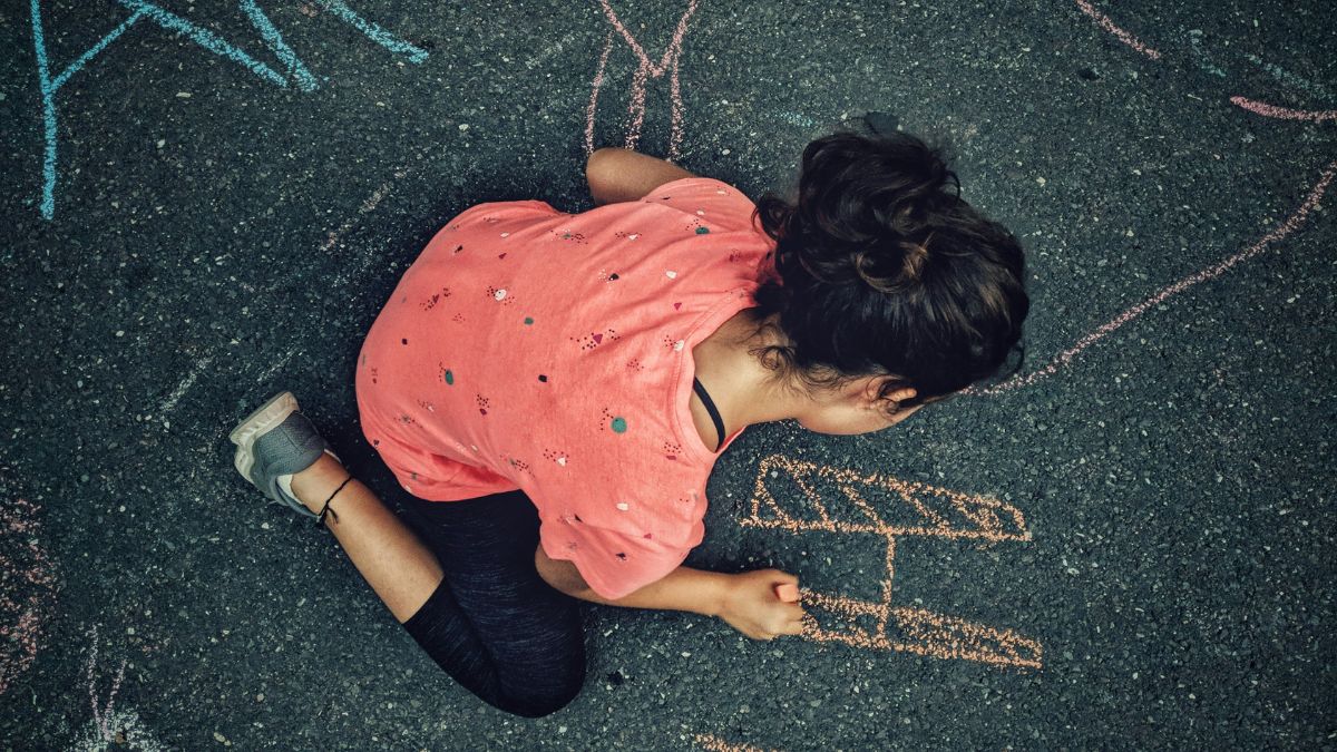 A young boy expressing his artistic spirit and independence, drawing vigorously with chalk on the street as a canvas.