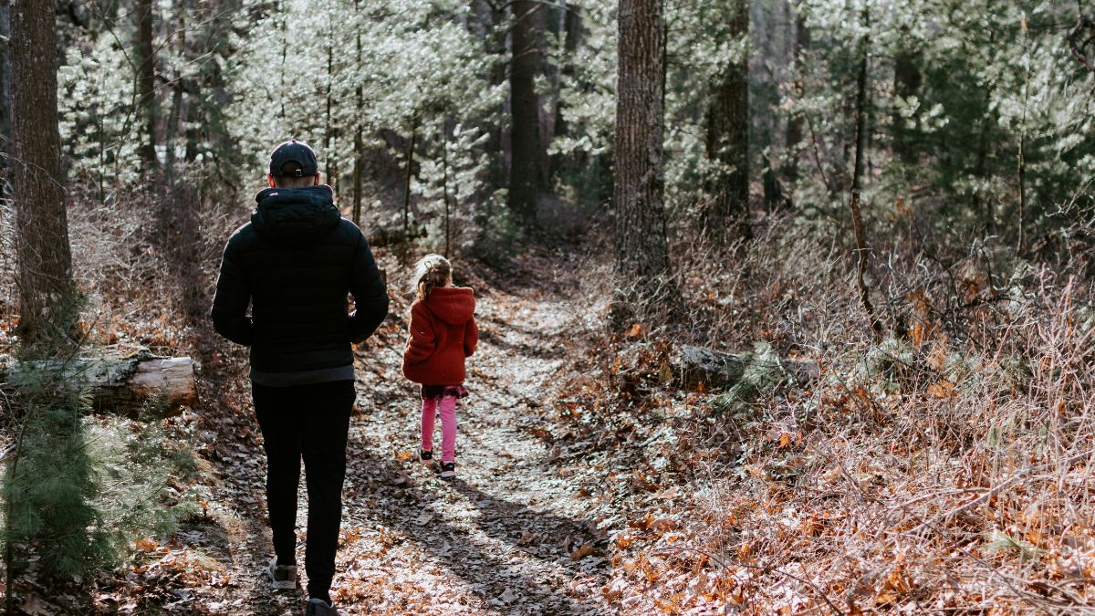 A young girl confidently walking ahead in the forest, guided by her father.