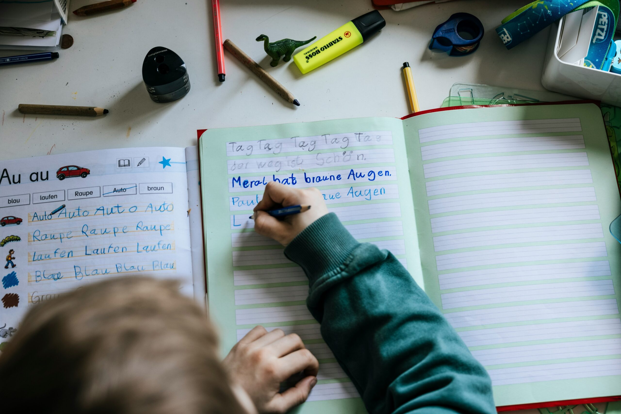 A child independently learning to write in cursive, using colored pencils on a notebook during an afternoon class.