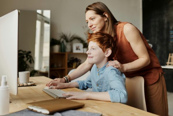 A child being guided on a computer at home by a therapist, looking happy and confident.