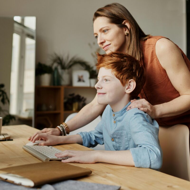 A child being guided on a computer at home by a therapist, looking happy and confident.
