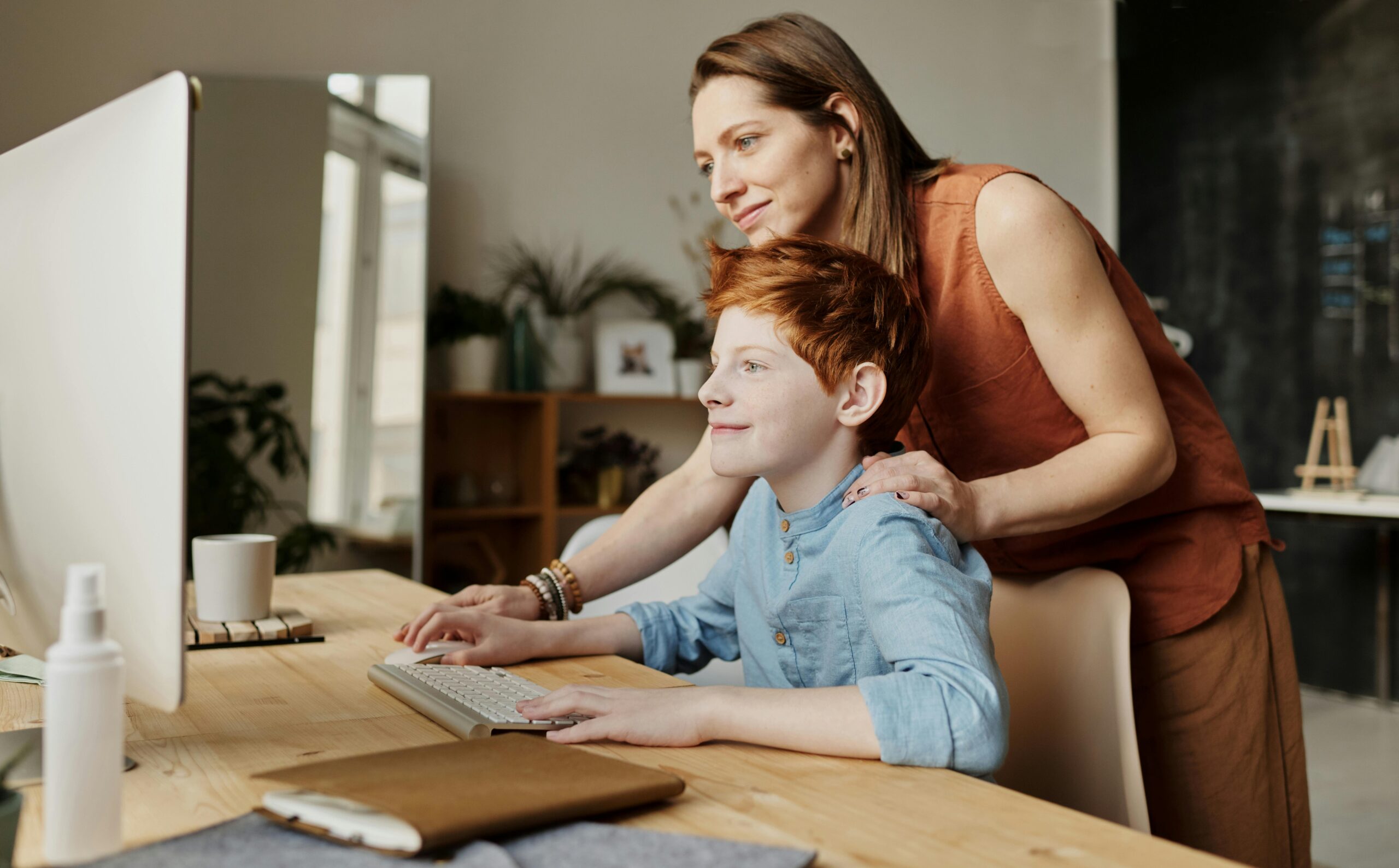 A child being guided on a computer at home by a therapist, looking happy and confident.