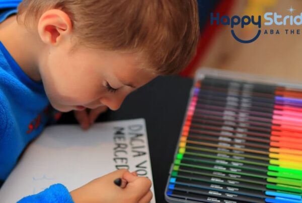 A blonde boy focuses on writing with colored pens, practicing despite writing letters backwards, as part of autism learning activities.