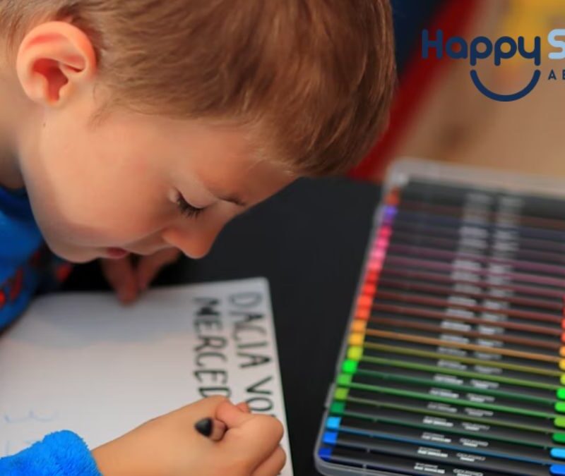 A blonde boy focuses on writing with colored pens, practicing despite writing letters backwards, as part of autism learning activities.