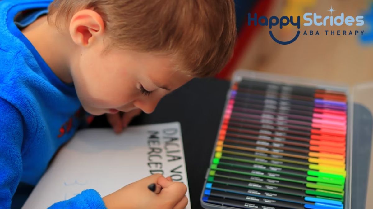 A blonde boy focuses on writing with colored pens, practicing despite writing letters backwards, as part of autism learning activities.