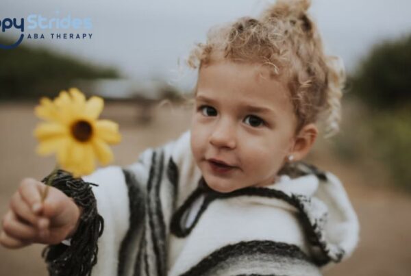 A young blonde girl with autism holds out a yellow daisy flower in the middle of a field under an overcast sky.