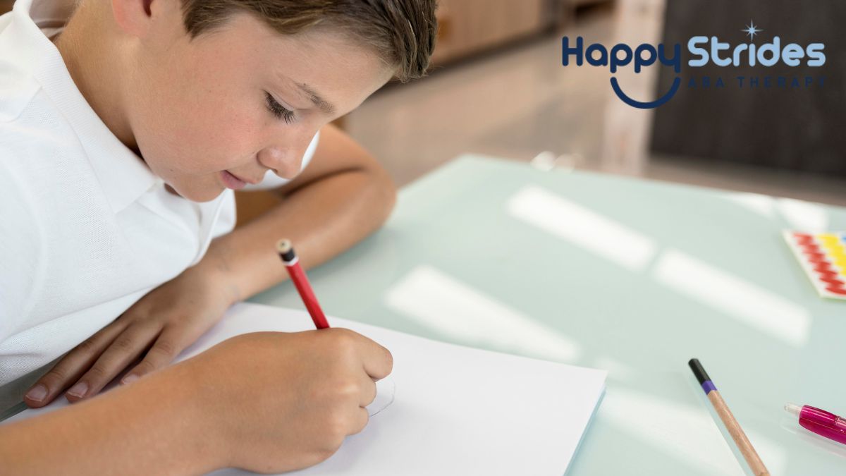 A boy bends over his notebook on a table, starting to write letters backwards, an activity linked to autism learning.
