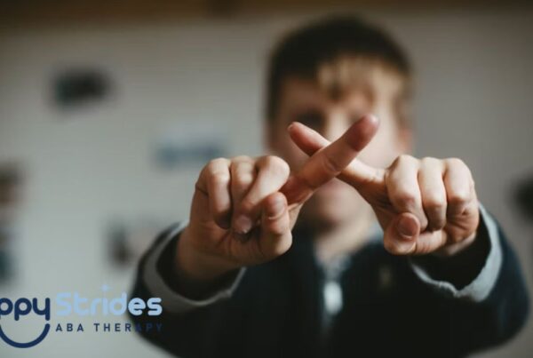 A young boy in blurred focus crosses his fingers in front of the camera to form an X, illustrating nonverbal communication in autism.