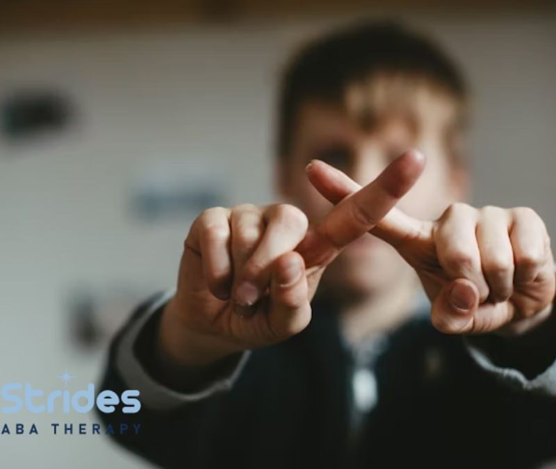 A young boy in blurred focus crosses his fingers in front of the camera to form an X, illustrating nonverbal communication in autism.