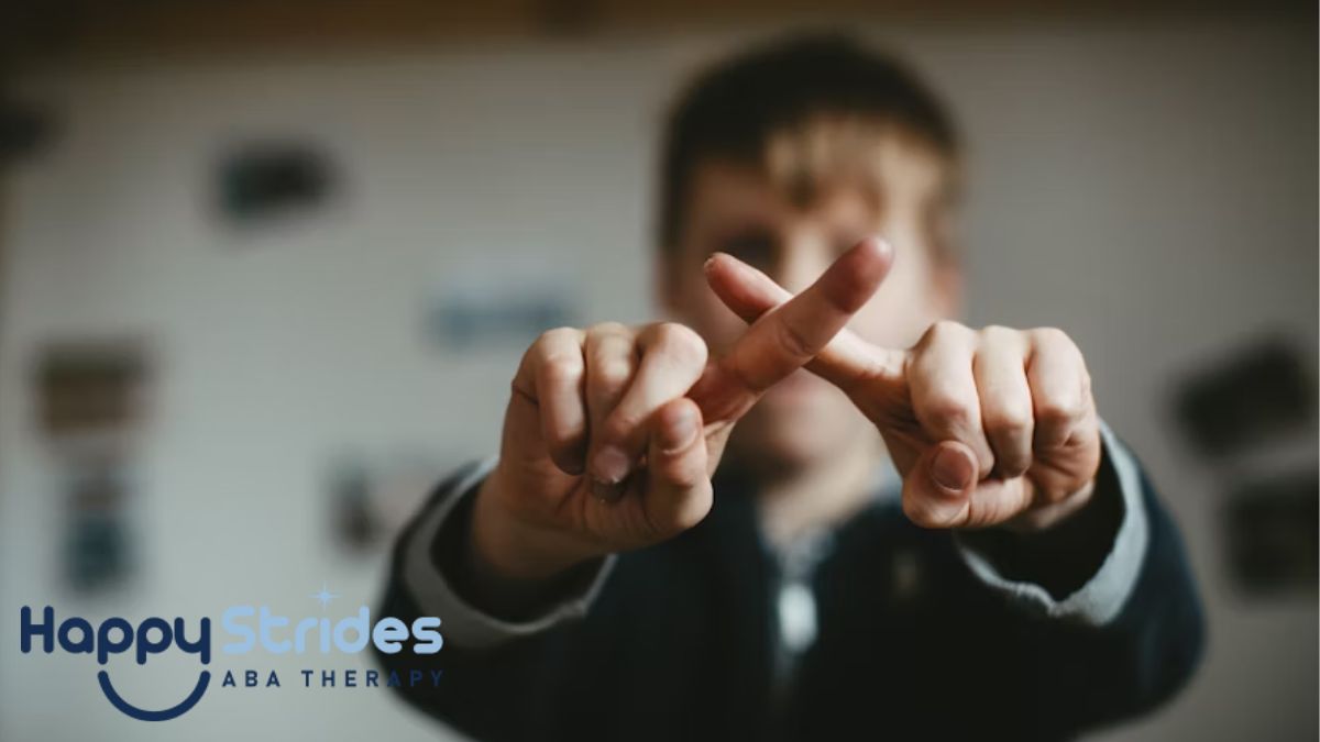 A young boy in blurred focus crosses his fingers in front of the camera to form an X, illustrating nonverbal communication in autism.