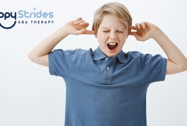 Hypersensitivity in autism, a boy in a blue shirt covers his ears while standing in a white room.