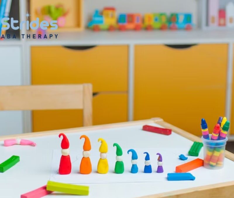 A row of plastic, colored gnomes arranged by height on a white table in a brightly lit playroom.