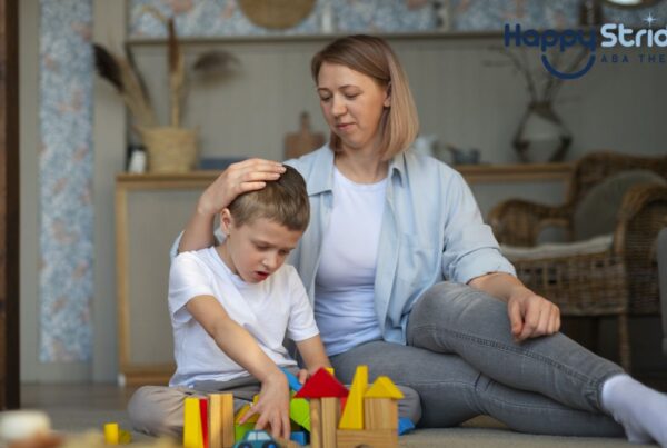 A female therapist or parent gently buzzes a young boy’s hair while holding him close during a play-based autism therapy session.