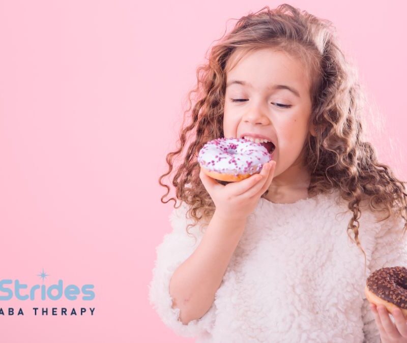 Autism and eating too much, a young child eats donuts voraciously while standing in a room with a pink background.