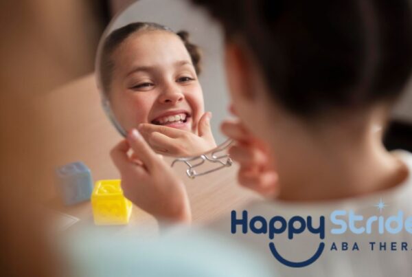 A young girl with braids smiles while looking into a hand mirror and examining her reflection during an autism self-help activity.