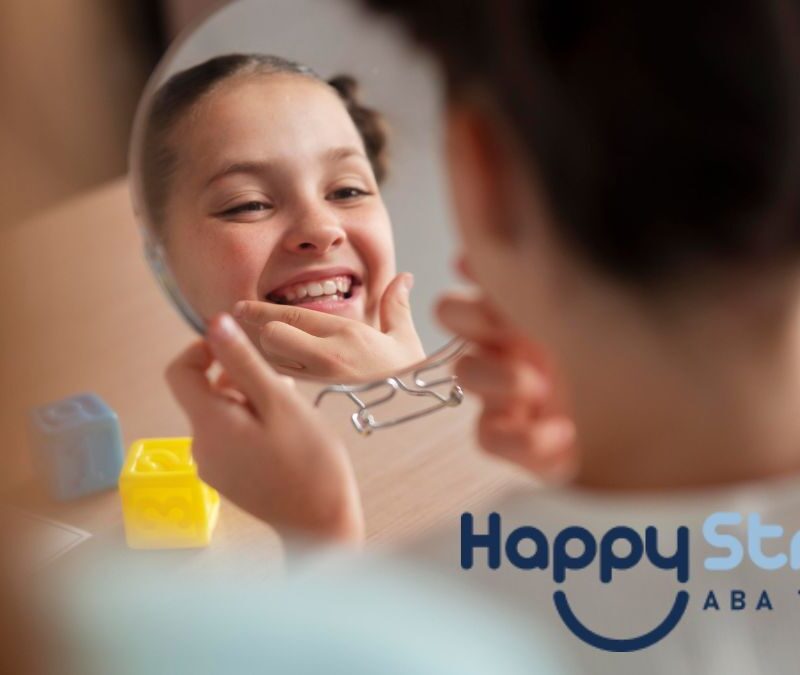 A young girl with braids smiles while looking into a hand mirror and examining her reflection during an autism self-help activity.