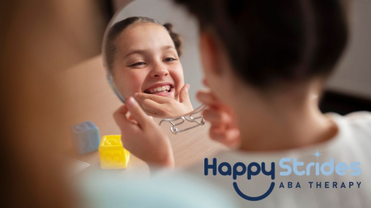 A young girl with braids smiles while looking into a hand mirror and examining her reflection during an autism self-help activity.