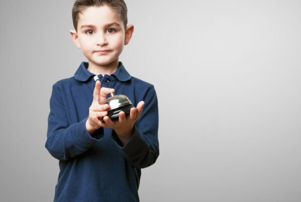 A young boy smiles at the camera while holding a chrome-plated training bell, showing excitement and engagement.