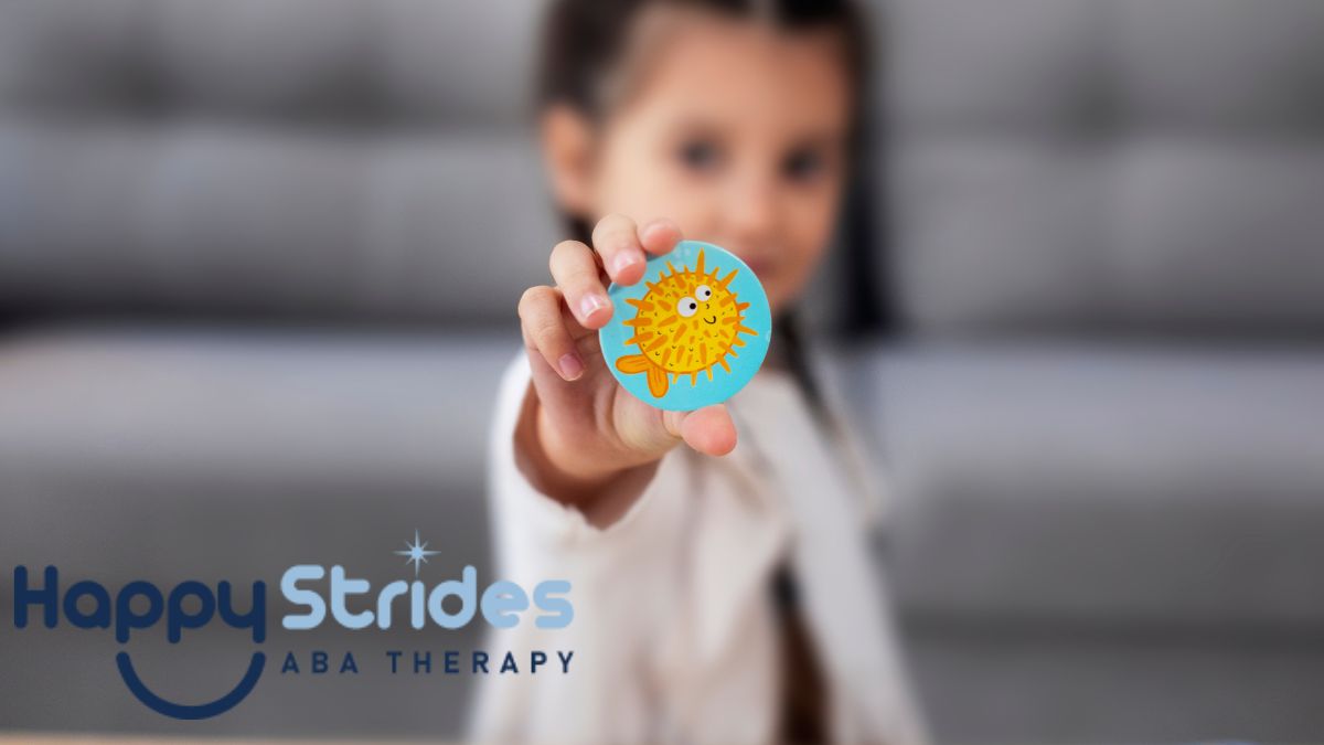 A young girl, slightly out of focus, holds up a cue card with a blowfish illustration during an autism self-help activity.