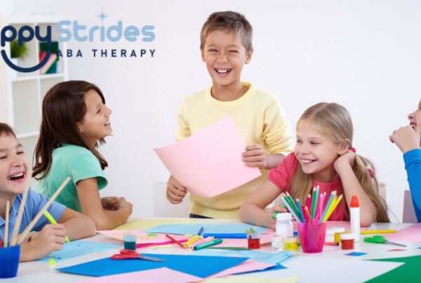 A group of children gather around a table in a white classroom, enjoying an activity together as they explore school and play items.