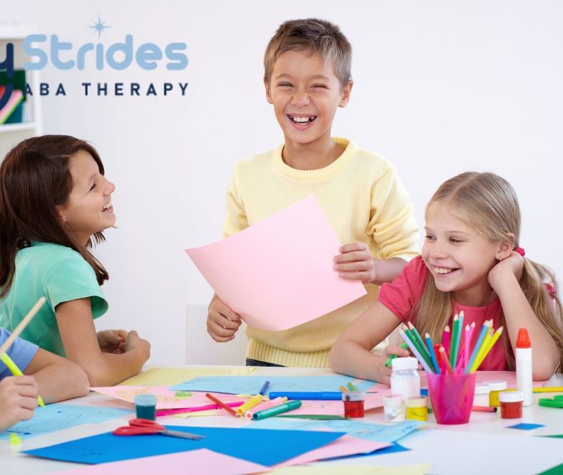 A group of children gather around a table in a white classroom, enjoying an activity together as they explore school and play items.