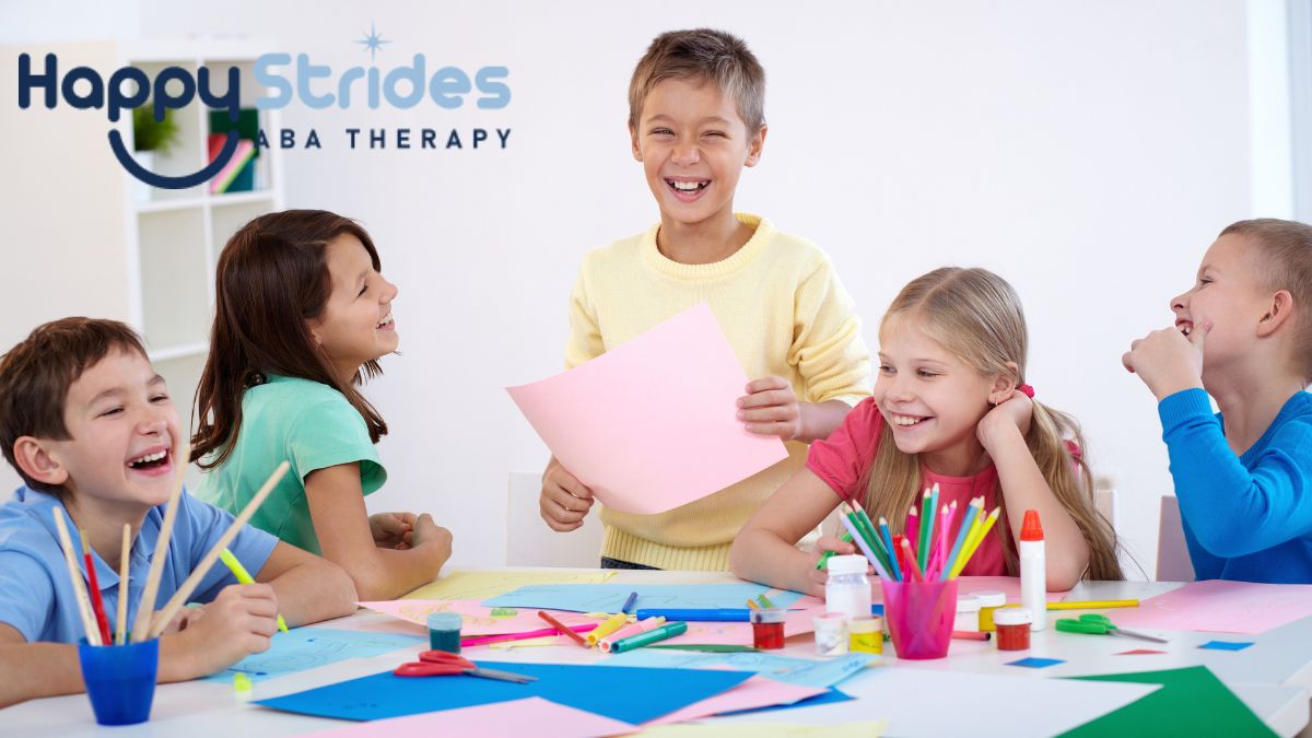 A group of children gather around a table in a white classroom, enjoying an activity together as they explore school and play items.
