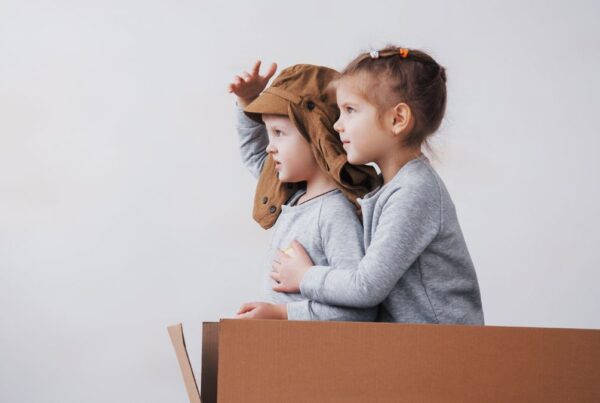 Two children in profile engage in a pretend play activity, imagining themselves as aviators, illustrating social interaction and transitional play often encouraged in autism support.
