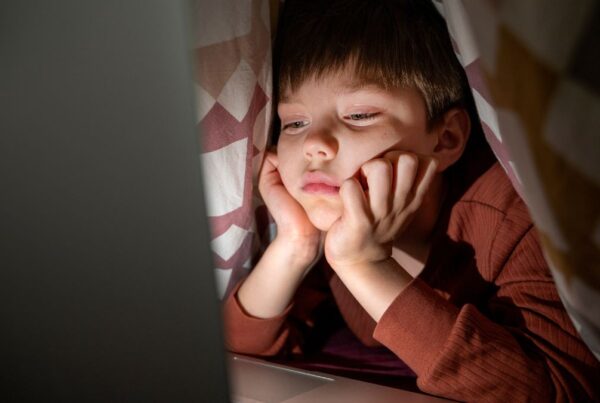 Boy staying up late while using a laptop, appearing tired in a dimly lit room.