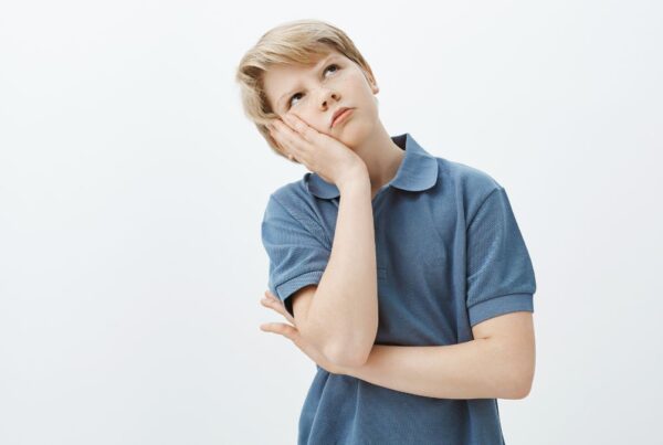 A young boy with autism rests his head on his palm and gazes to the right with a wondering, slightly anxious expression.