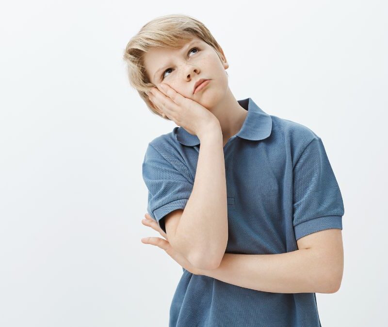 A young boy with autism rests his head on his palm and gazes to the right with a wondering, slightly anxious expression.