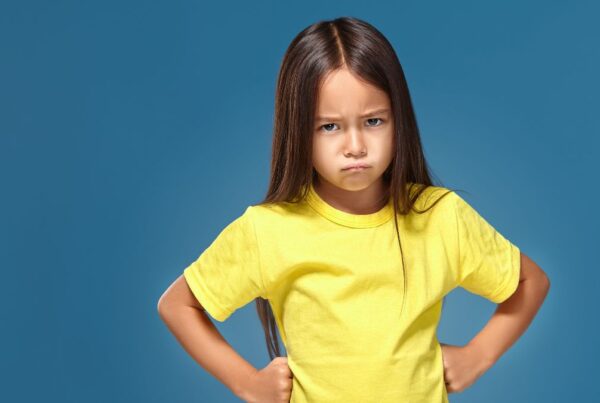 A young girl with autism wearing a yellow shirt frowns at the camera, showing signs of emotional awareness.