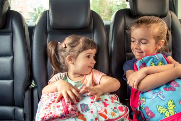 Two children ride a bus together, holding their backpacks, representing everyday transitions and shared routines often discussed in autism support.