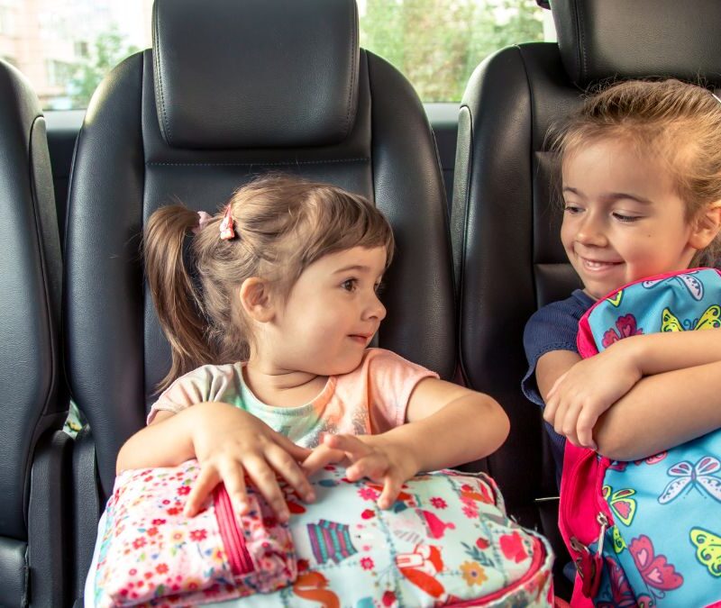 Two children ride a bus together, holding their backpacks, representing everyday transitions and shared routines often discussed in autism support.