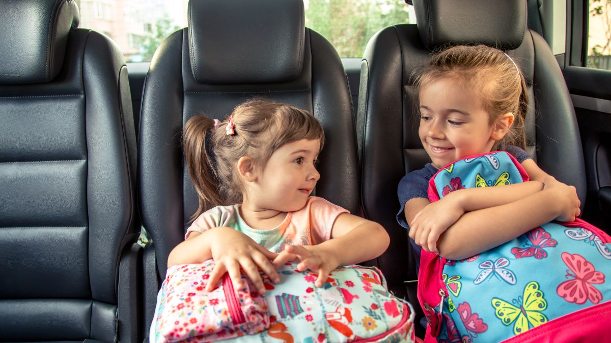 Two children ride a bus together, holding their backpacks, representing everyday transitions and shared routines often discussed in autism support.