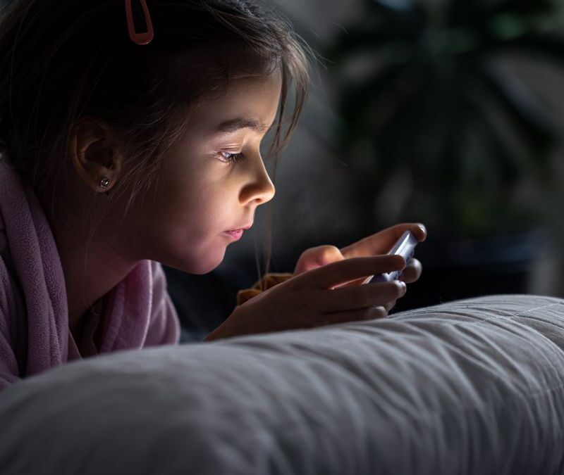 Girl staying up late reading from a smartphone, illustrating sleep challenges often discussed in autism.